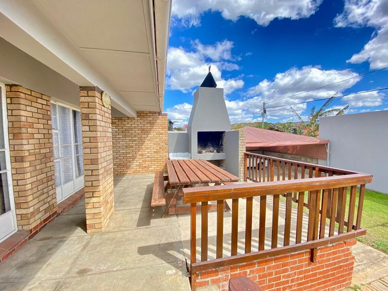 Covered patio area featuring a built-in braai, brick structural pillars, and a timber balustrade overlooking the garden.