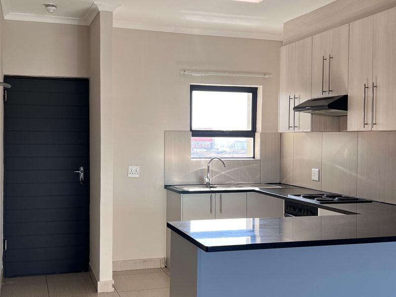 Modern kitchen featuring light wood cabinetry, dark granite countertops, integrated hob, extractor fan, and neutral tiled flooring in an open-plan layout.