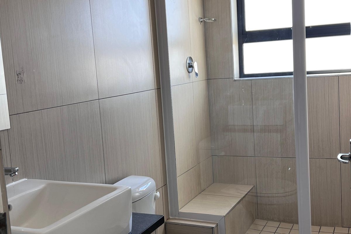 Modern bathroom featuring a vanity with countertop basin, toilet, and a walk-in shower with a glass screen and tiled finishes.