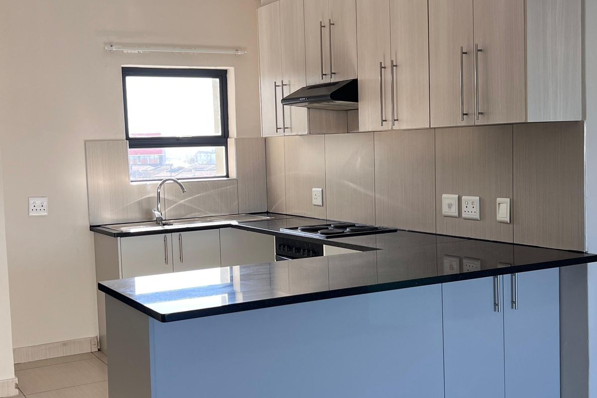 A modern, clean kitchen featuring light wood-finish cabinetry, dark granite countertops, a built-in hob, extractor fan, and neutral tiled flooring.