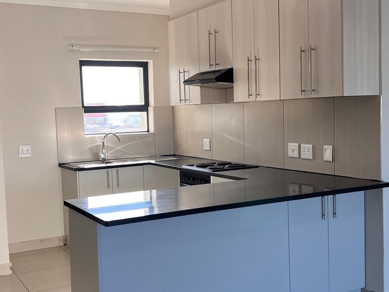 A modern, clean kitchen featuring light wood-finish cabinetry, dark granite countertops, a built-in hob, extractor fan, and neutral tiled flooring.