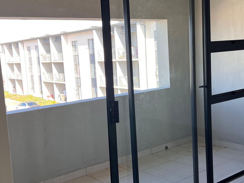 A covered balcony featuring tiled flooring and a sliding glass door, offering an outdoor space with views of the surrounding apartment complex.