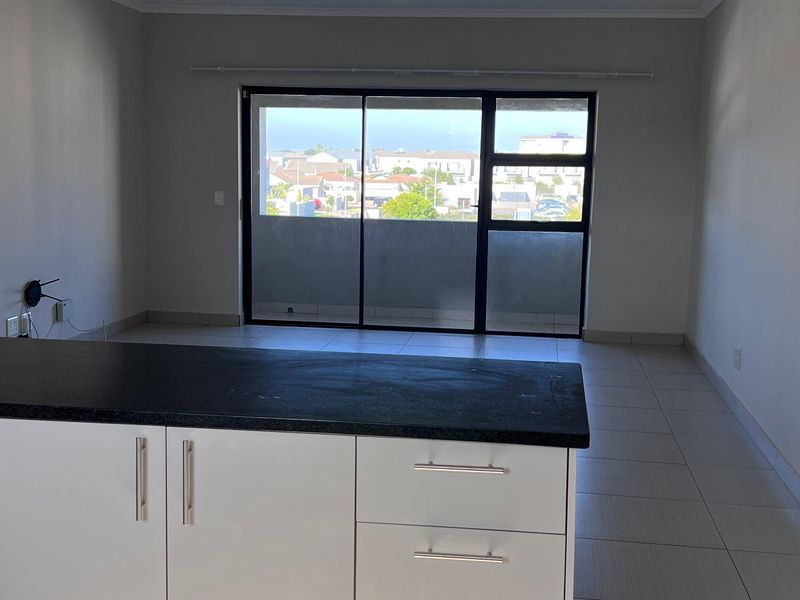 An open-plan living and kitchen area featuring a central island with stone countertops, tiled flooring, and large sliding doors leading to a balcony.