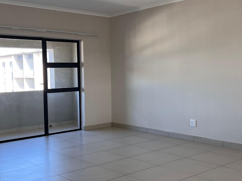 A bright, empty living area featuring neutral tiled flooring and a large sliding glass door providing access to an outdoor space.