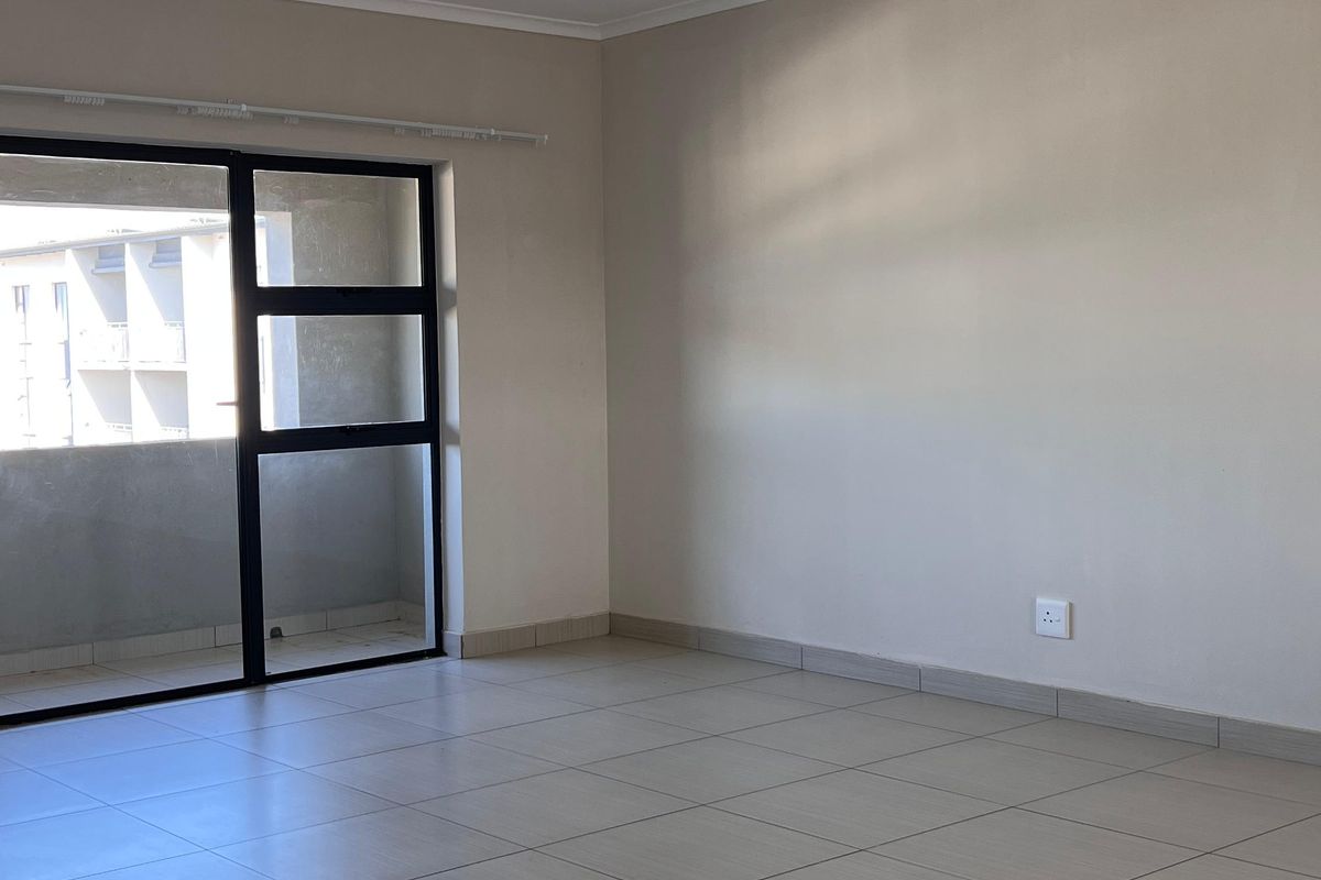 A bright, empty living area featuring neutral tiled flooring and a large sliding glass door providing access to an outdoor space.