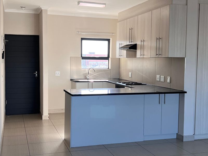 Modern open-plan kitchen featuring light-toned cabinetry, granite countertops, integrated hob, and tiled flooring in a clean, well-maintained apartment setting.