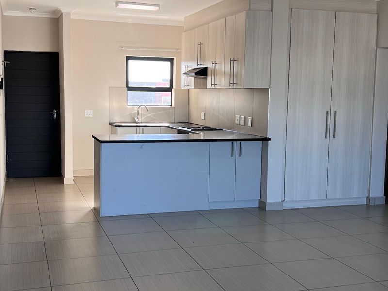 Open-plan living area featuring a modern kitchen with built-in cabinetry, a functional island, and neutral tiled flooring throughout.