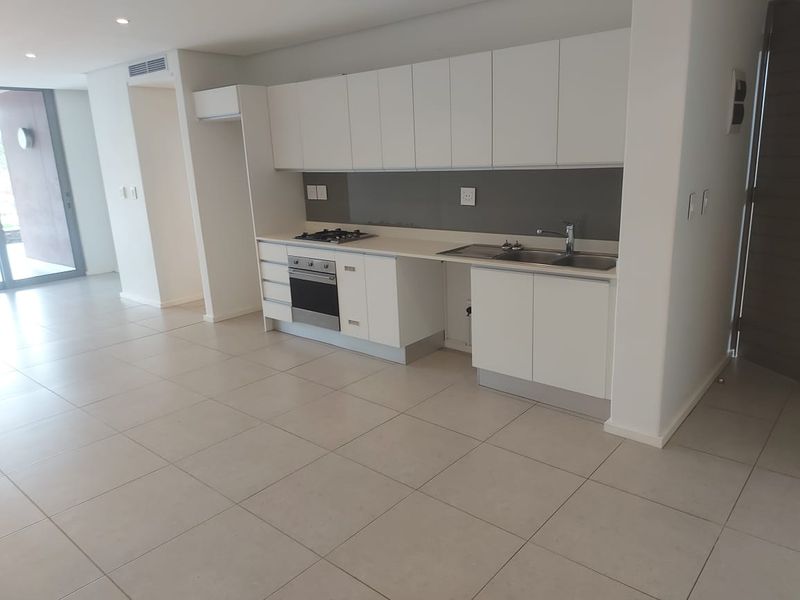 Modern, minimalist kitchen featuring white cabinetry, integrated gas hob, electric oven, and neutral tiled flooring in an open-plan layout.