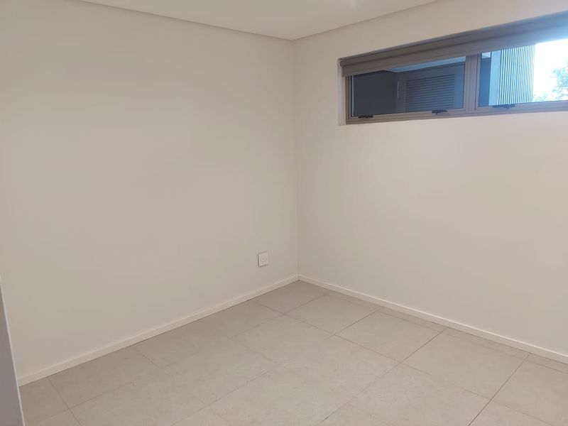 A clean, empty bedroom featuring neutral tiled flooring, white walls, and a modern aluminium window with a fitted roller blind.