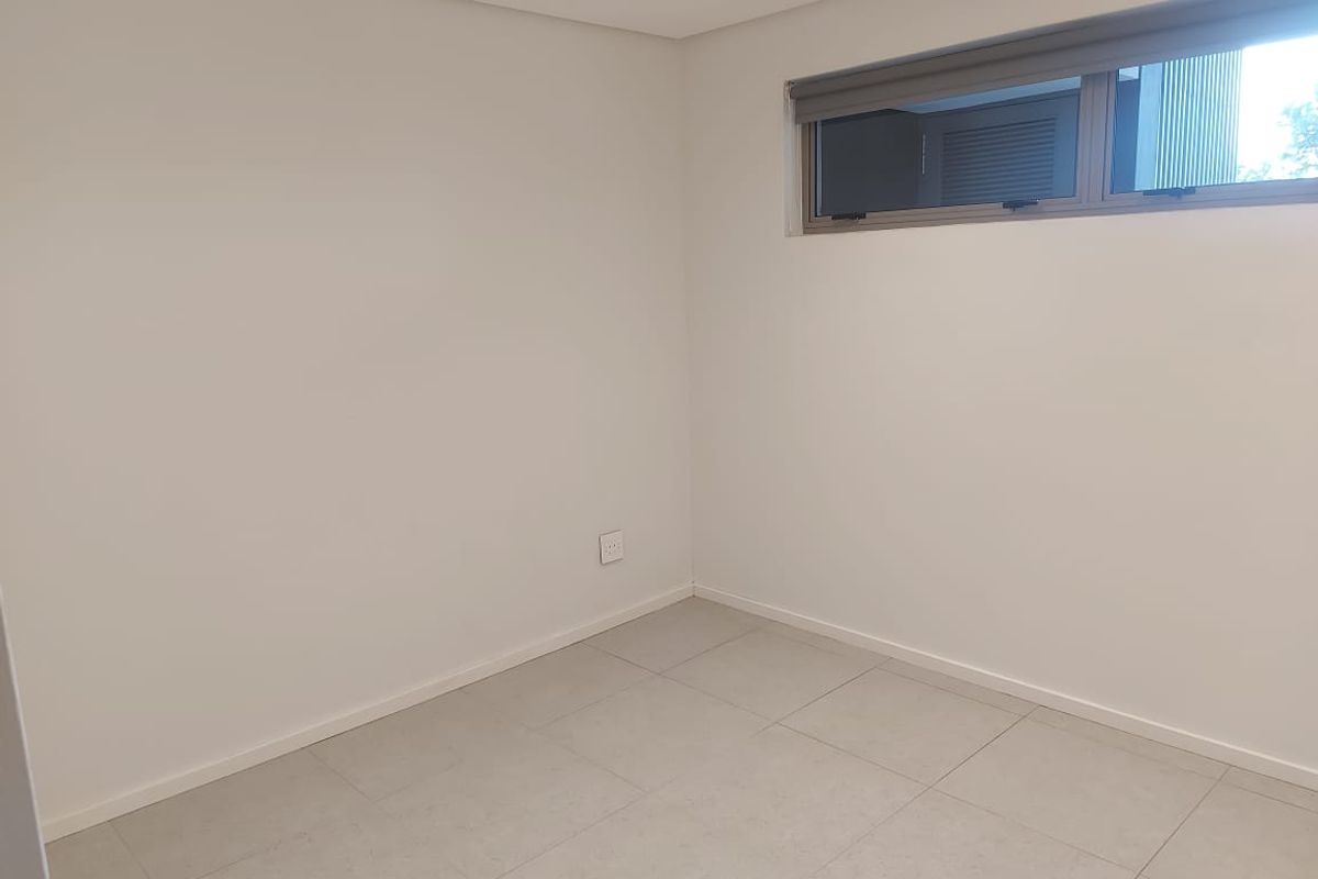 A clean, empty bedroom featuring neutral tiled flooring, white walls, and a modern aluminium window with a fitted roller blind.