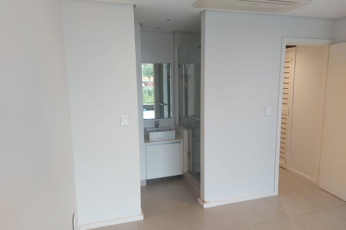 A modern, minimalist bathroom featuring a floating vanity with a vessel sink, a glass-enclosed shower, and integrated ceiling air conditioning.