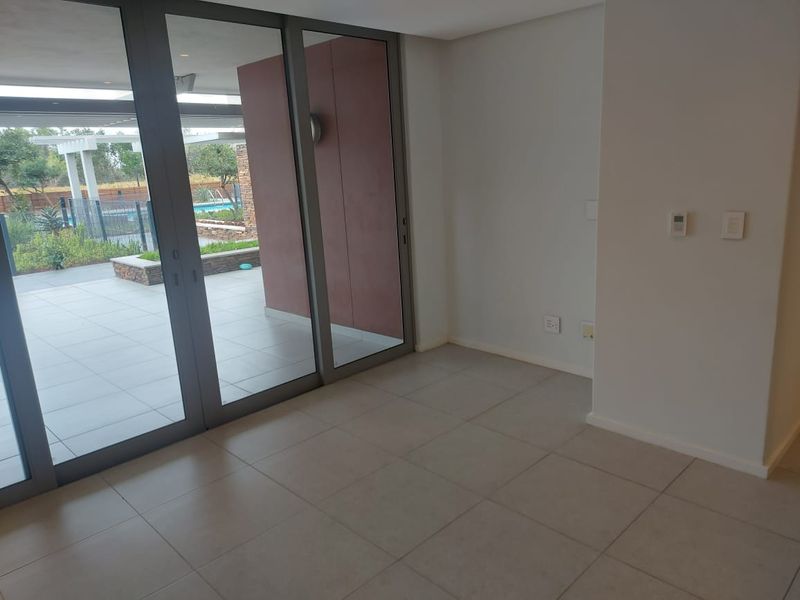 A bright, empty living area featuring large sliding glass doors that open onto a patio, with neutral tiled flooring and modern finishes.