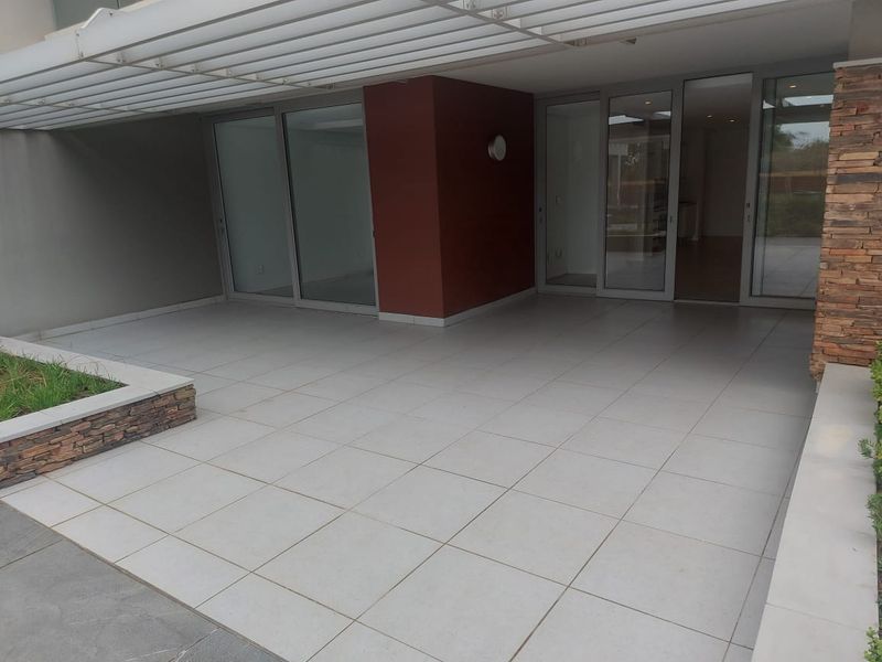 A spacious covered patio featuring modern light-colored floor tiles, stone cladding accents, and large sliding glass doors providing seamless indoor-outdoor flow.