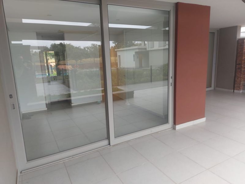 A spacious, covered patio area featuring large sliding glass doors, neutral tiled flooring, and modern recessed ceiling lighting.