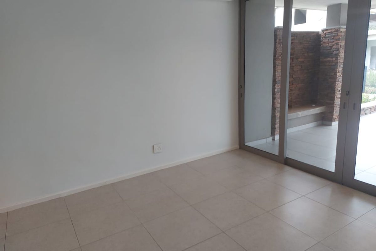 A bright, empty living area featuring neutral tiled flooring and large sliding glass doors that open onto a private patio.