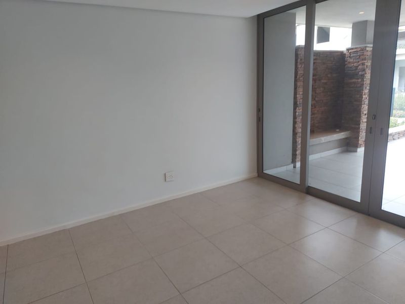 A bright, empty living area featuring neutral tiled flooring and large sliding glass doors that open onto a private patio.