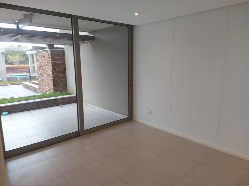 Bright, empty living area featuring large sliding glass doors that open onto a private patio, finished with neutral floor tiles and recessed lighting.