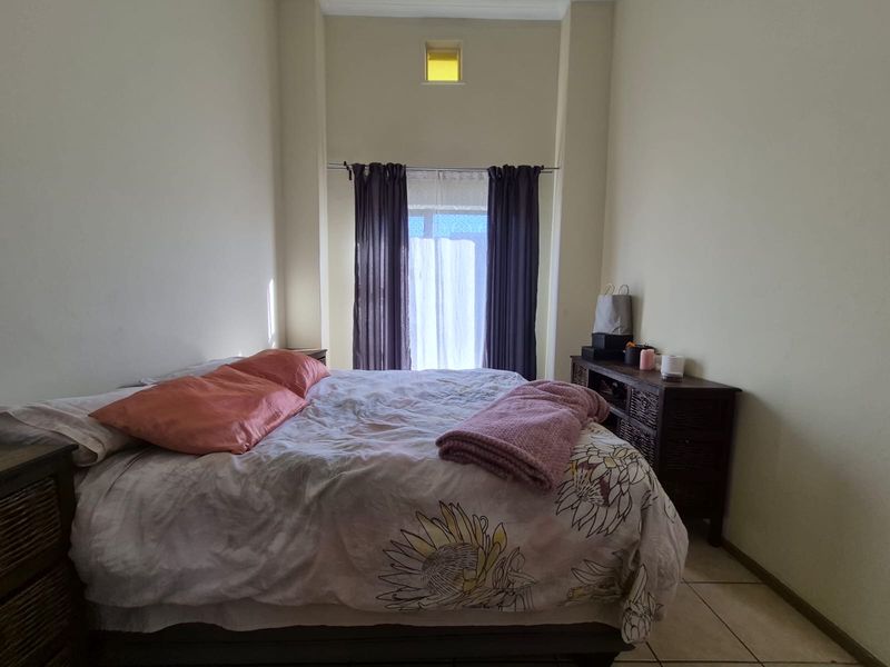 A bedroom featuring tiled flooring, a small high-level window, and a curtain rod, providing a functional space with neutral wall finishes.