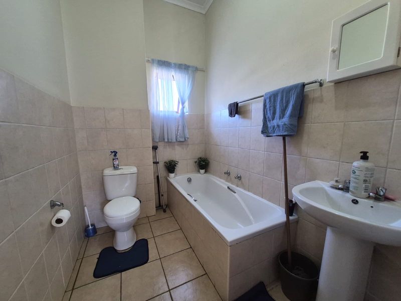 A functional bathroom featuring a bathtub, pedestal basin, and toilet with neutral wall and floor tiling.