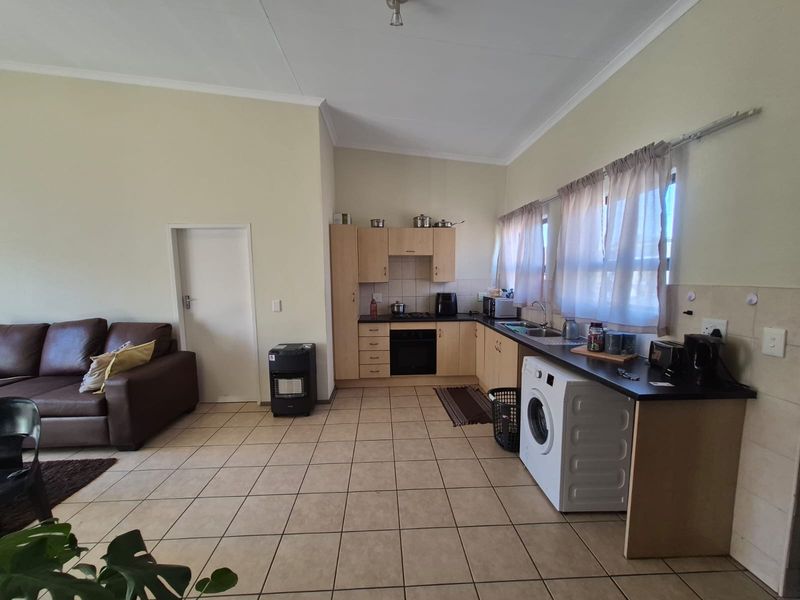 An open-plan living and kitchen area featuring tiled flooring, light wood cabinetry, built-in oven and hob, and a functional laundry space under the counter.