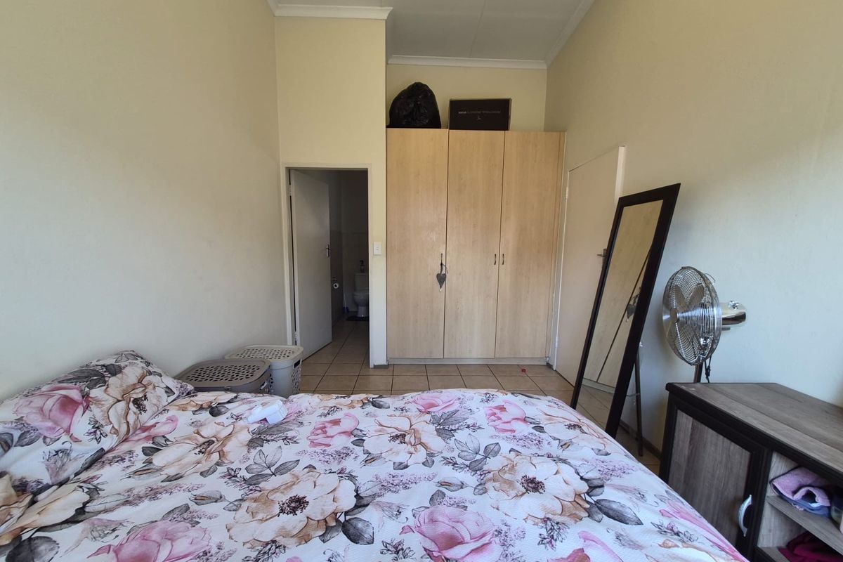 A bedroom featuring built-in wooden wardrobes, tiled flooring, and a coved ceiling, with an adjoining doorway leading to an en-suite bathroom.