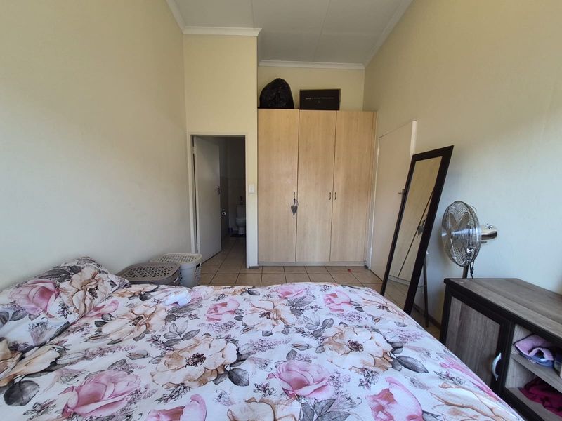 A bedroom featuring built-in wooden wardrobes, tiled flooring, and a coved ceiling, with an adjoining doorway leading to an en-suite bathroom.