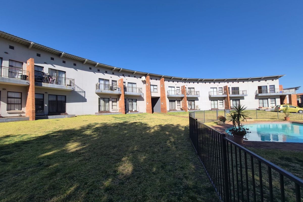 Rear view of the apartment complex featuring a communal swimming pool, landscaped lawn area, and private balconies for each unit.
