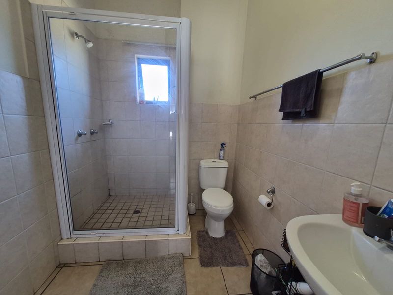 A functional bathroom featuring a shower enclosure, pedestal basin, and toilet with neutral wall and floor tiling.