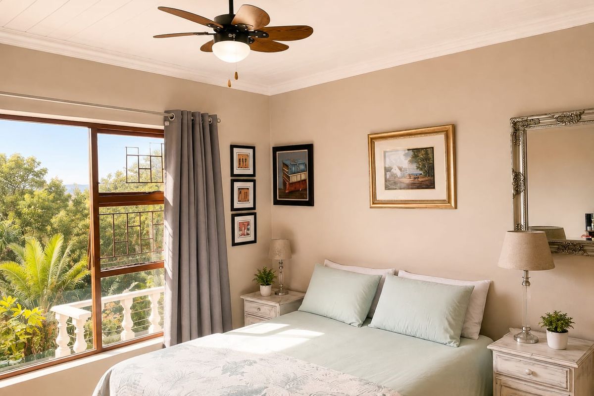 A well-maintained bedroom featuring a ceiling fan, coving, and large windows with views of the surrounding greenery and a balcony balustrade.