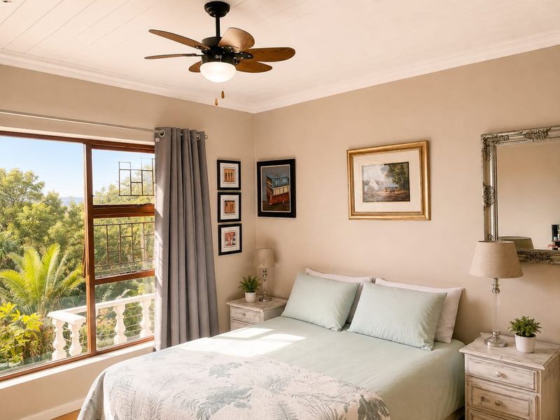 A well-maintained bedroom featuring a ceiling fan, coving, and large windows with views of the surrounding greenery and a balcony balustrade.