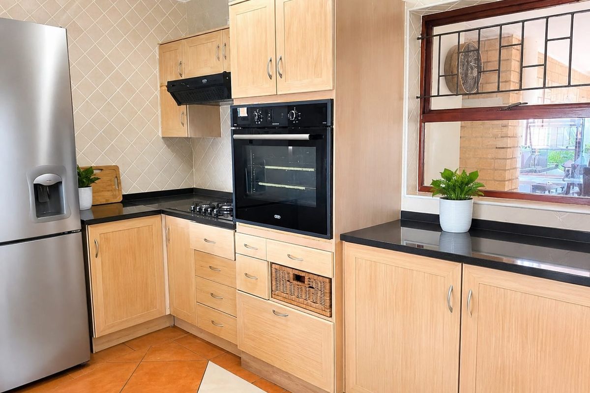 A functional kitchen featuring light wood cabinetry, black granite countertops, a built-in oven, gas hob, and a tiled backsplash.
