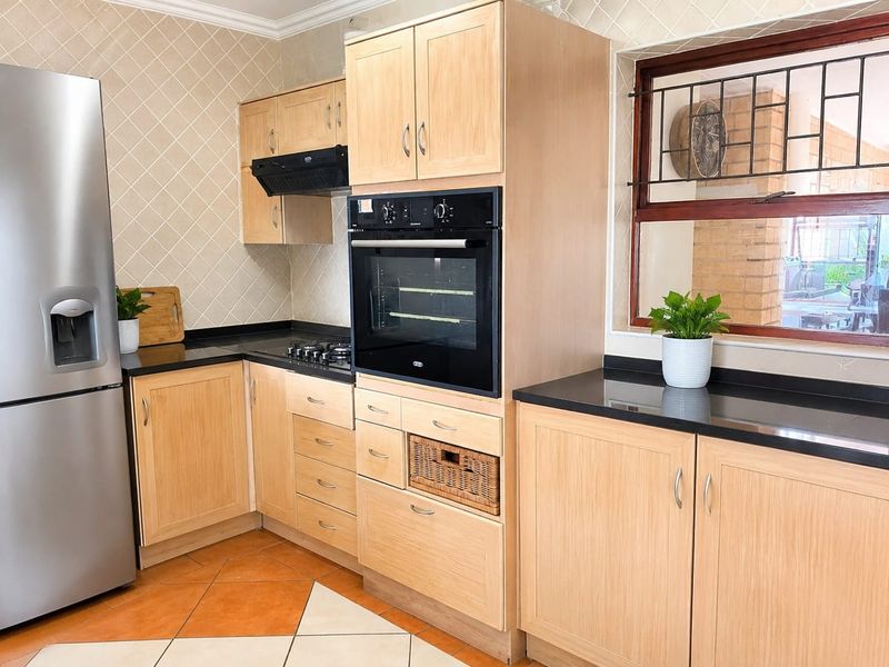 A functional kitchen featuring light wood cabinetry, black granite countertops, a built-in oven, gas hob, and a tiled backsplash.