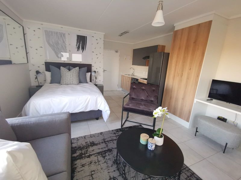 A modern open-plan studio apartment featuring a combined sleeping and living area with a compact kitchenette and built-in storage.