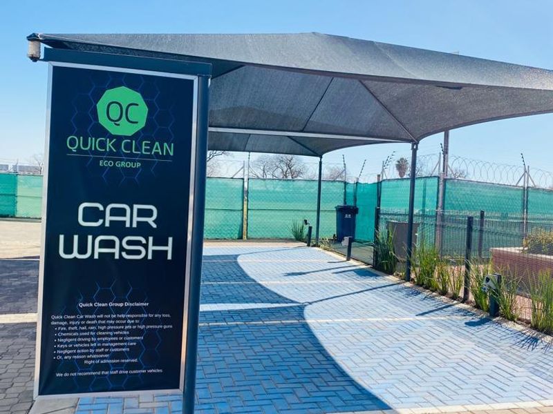 A dedicated outdoor car wash bay featuring paved flooring, shade netting structure, and secure perimeter fencing within the apartment complex.