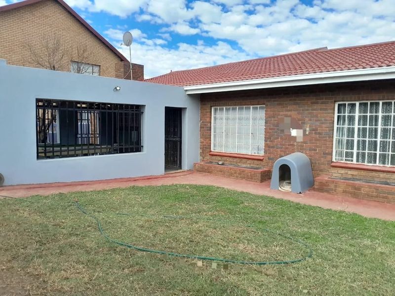 Rear view of the property featuring a brick facade, tiled roof, security-barred windows, and a private garden area.
