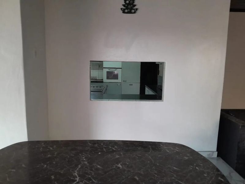 A view through a kitchen pass-through window showing built-in cabinetry and an oven, with a dark marble-effect countertop in the foreground.