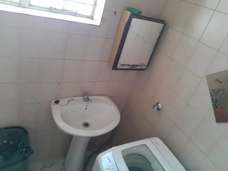 A functional laundry area featuring a pedestal basin, tiled walls, and a wall-mounted cabinet, requiring cosmetic updates to improve its overall condition.