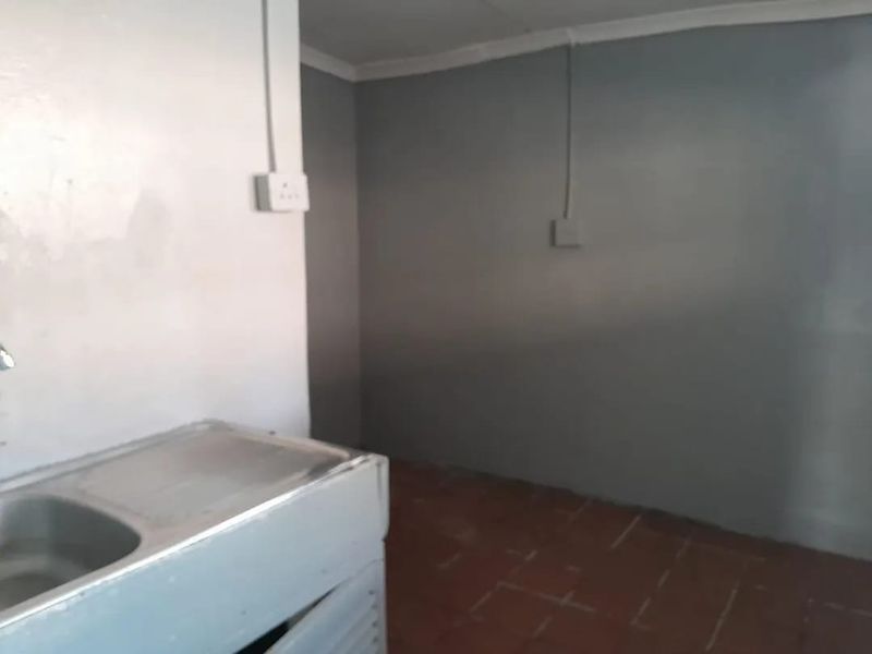 A basic, empty kitchen area featuring a stainless steel sink, tiled flooring, and simple wall finishes, suitable for renovation or modernization.