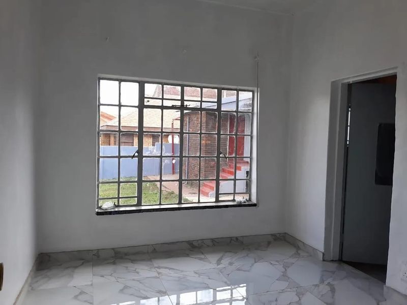 An empty living room featuring large steel-framed windows and modern marble-look floor tiles, offering a bright and neutral space ready for personalization.