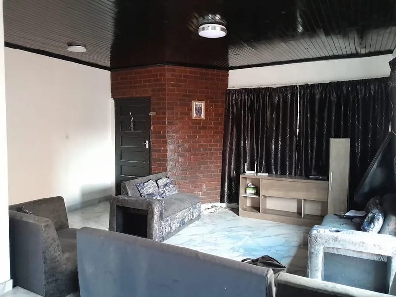 Living room featuring an exposed brick wall, glossy timber-look ceiling, and tiled flooring, offering a dated aesthetic ready for modernization.