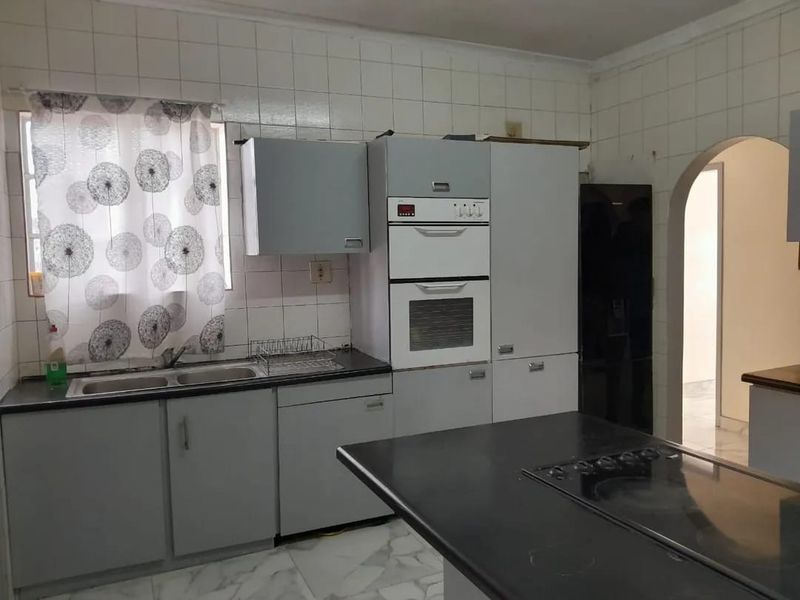 Functional kitchen featuring built-in oven, ceramic hob, double sink, and ample cabinetry with tiled splashbacks and stone countertops.
