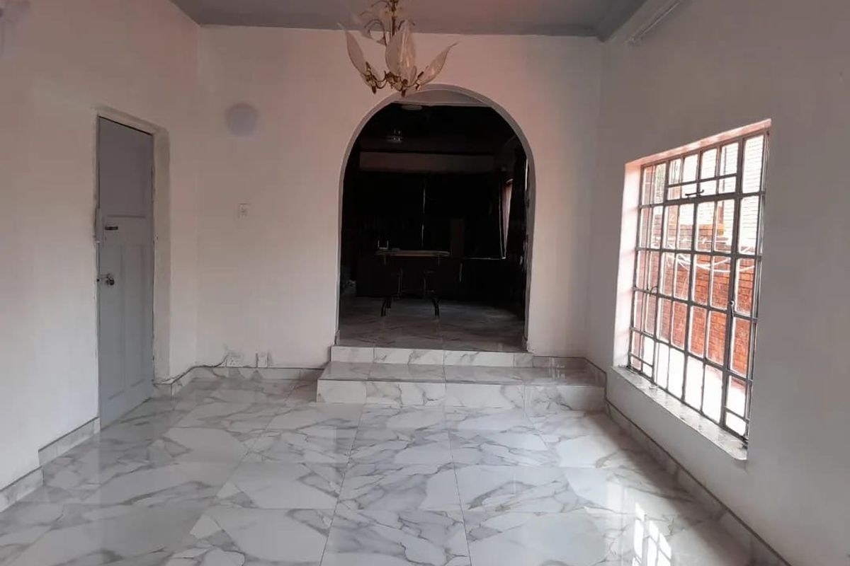 An empty living room featuring marble-look floor tiles, an arched doorway leading to an adjacent space, and a window with security bars.