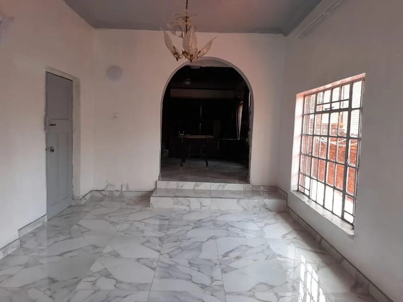An empty living room featuring marble-look floor tiles, an arched doorway leading to an adjacent space, and a window with security bars.