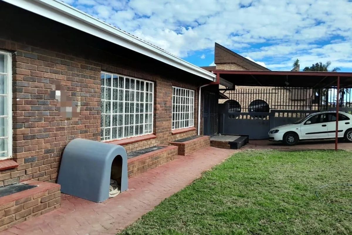 Rear view of a face brick house featuring a paved walkway, lawn area, and a covered carport structure.