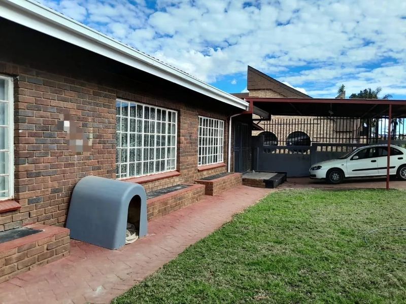 Rear view of a face brick house featuring a paved walkway, lawn area, and a covered carport structure.
