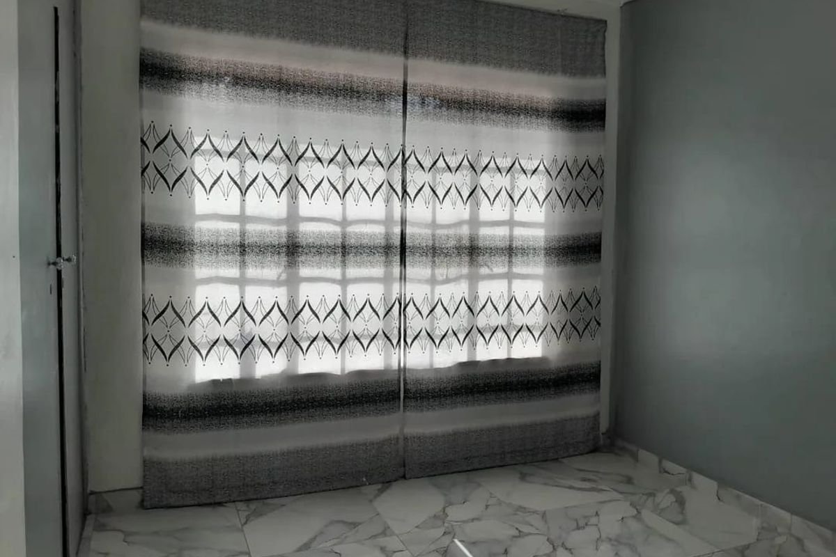 A bright, empty bedroom featuring modern marble-look floor tiles and a large window with security bars.