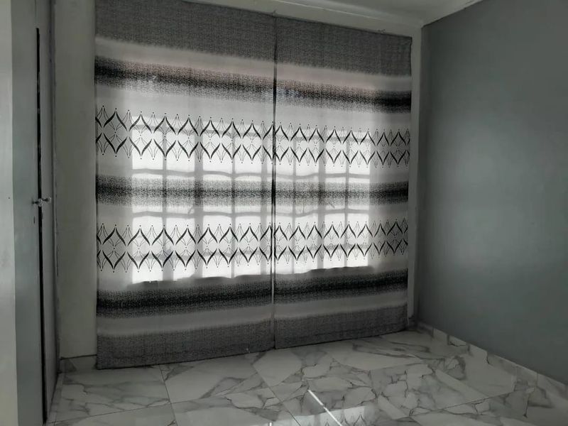A bright, empty bedroom featuring modern marble-look floor tiles and a large window with security bars.