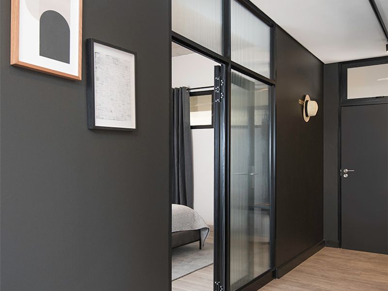 Modern hallway featuring dark charcoal walls, light wood-look flooring, and a stylish fluted glass partition leading into the bedroom.
