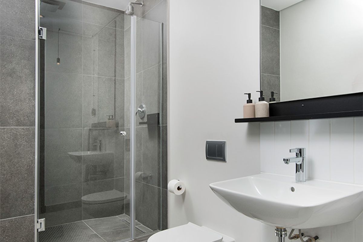 Modern bathroom featuring a glass-enclosed shower, wall-mounted toilet, and sleek basin with contemporary grey and white tiling.