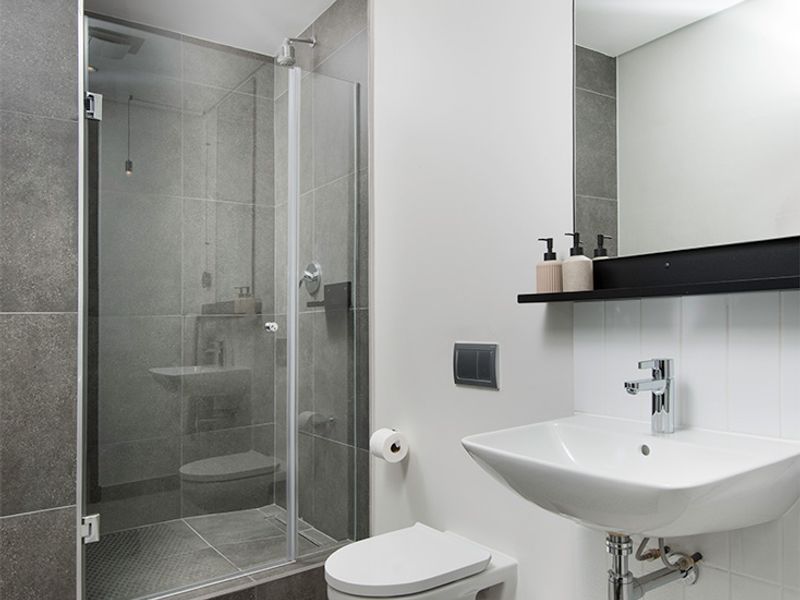 Modern bathroom featuring a glass-enclosed shower, wall-mounted toilet, and sleek basin with contemporary grey and white tiling.